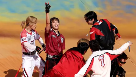 Members of BTS dance and gesture while wearing red shirts performing at the soccer World Cup final in 2026