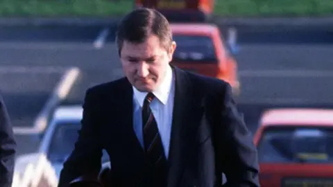 Pacemaker Pat Finucane, a man with dark hair, wearing a black jacket, white shirt and black and red tie.