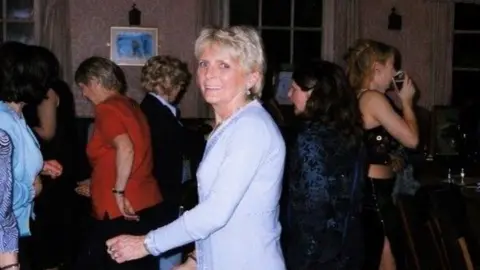 Whitehurst Family Jackie Whitehurst is on the dancefloor at a party. She is smiling at the camera and is wearing a blue dress. 