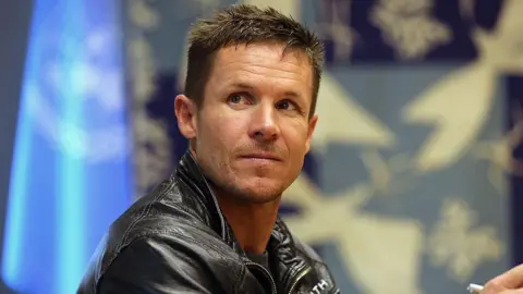 Felix Baumgartner looks off to the side. He has blue eyes and short brown hair. He is wearing a leather jacket.