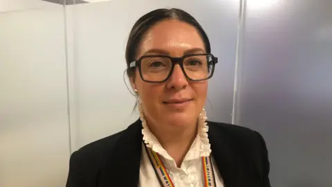 Camilla Barrow wearing black-framed glasses and a white collared top and black jacket.