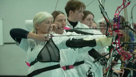 A line of people dressed in white, shooting arrows 