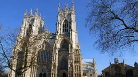 The 15th-century, gothic-style western towers of York Minster under a clear blue sky.