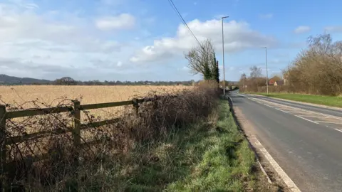 A field with a wooden fence next to a two-lane road