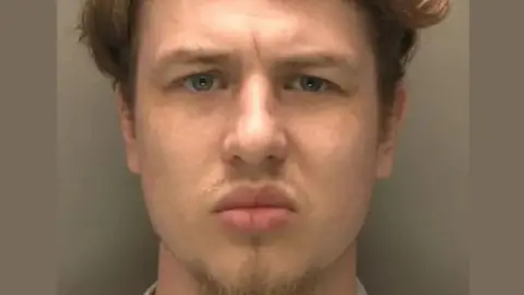 A police mugshot of Owen Blades. He has mousey-brown-blond hair and blue eyes, and is looking directly at the camera.