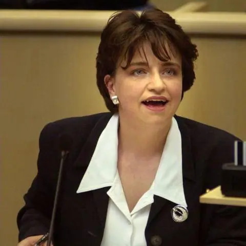 PA Media A young Wendy Alexander in 2000 in the debating chamber of the Scottish Parliament. She is sitting at a pale wood desk, and is wearing a white shirt and black jacket with a circular silver brooch.
