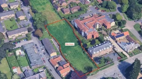 An aerial view of planning application site. It shows a large green field with houses surrounding it. The development area is indicated with a red border drawn around it with the words 'site area'.