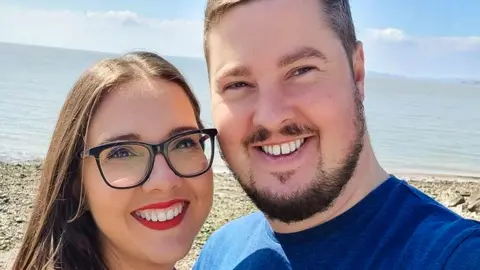 Julian Morgan Julian and his partner smile in a selfie. they are on a beach 