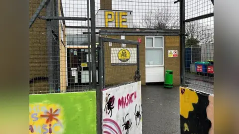 An external image of the Pie Factory at Ramsgate Youth Centre. The building has two signs stating 'Pie' - one larger on the roof and one to the right of the front door. The gate entrance features a number of paintings.