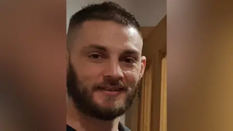 A picture of Matthew Schofield standing in a doorway. The image has been cropped with a blurred background.