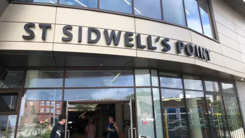 The entrance to the St Sidwell's Point leaiure centre with people going into and out of the building
