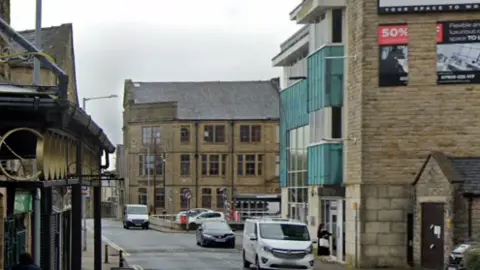 A white van parked on Cross Street in the centre of Nelson with shops and stone buildings either side