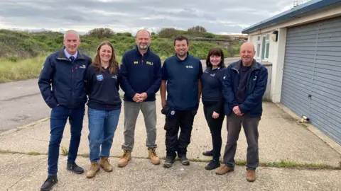 Four men and two women from the lifeboat crew at Spurn Point. They are standing outside the former station in RNLI dark blue branded clothing. 