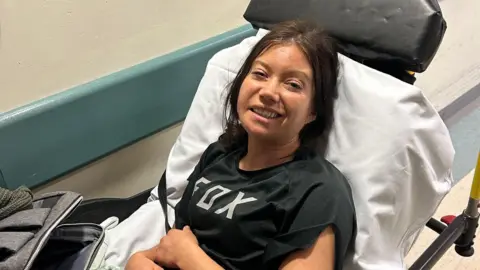 supplied Cara Grimwade sat in a hospital bed wearing a black t-shirt