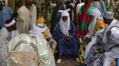 Traditional Nigeria leaders in their traditional clothes sit in a circle.