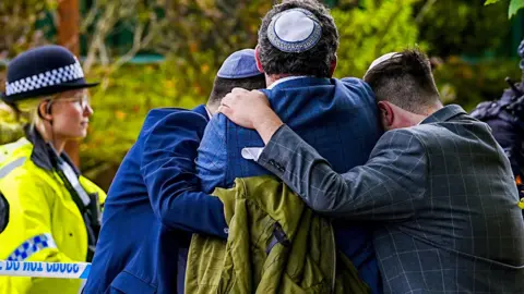 Worshippers console each other after the attack o0n their synagogue while a police officer looks on.