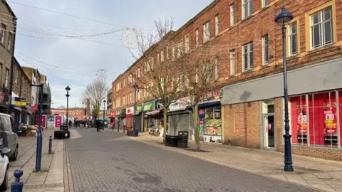 Gemma Dillon/BBC Image shows a pedestrian street.
It is empty and shows several closed or boarded up shops.
There are lamp posts and trees down either side of the street. 