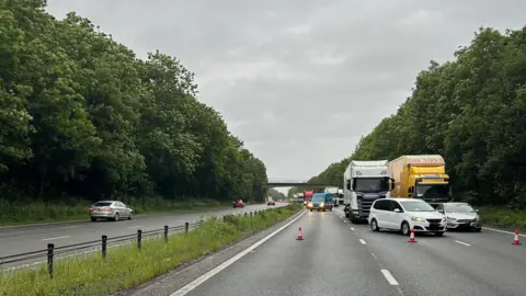 Both carriageways, both being three lanes, are visible in the image, with the right hand carriageway featuring cones holding up vehicles.
