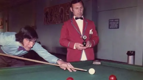 Simon McDermott A photo from the 60s or 70s showing Ted in his Butlin's red jacket holding a trophy as a man in a blue shirt and purple bow tie cues up a snooker shot