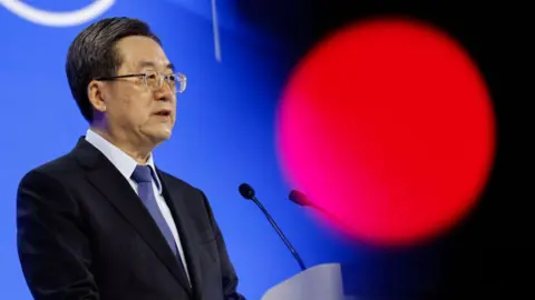 Ding Xuexiang, China's first vice premier, in a suit and tie stands at a podium with a microscope to address the World Economic Forum (WEF) in Davos, Switzerland, on Tuesday, Jan. 21, 2025