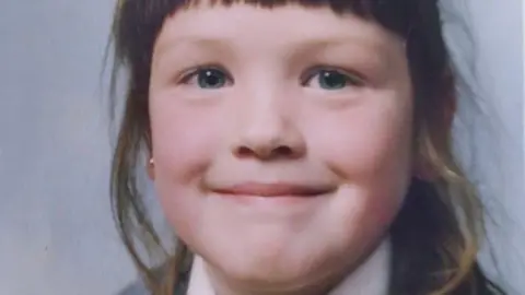 Sinead Quinn as a child. It is a close up. She is grinning and has a blunt fringe in what is a primary school picture.