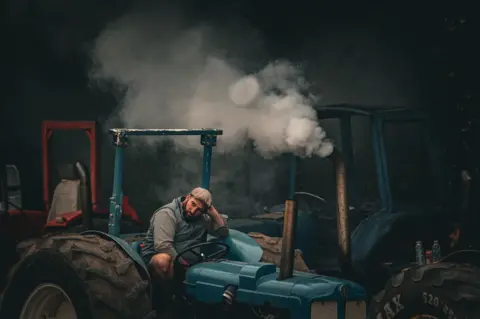 Bobby Ford A husbandman  sits connected  his tractor with fume  coming from the exhaust