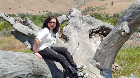 Teenage girl sat on a fallen tree with sun-bleached bark.