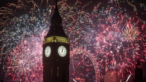 Big Ben in Westminster at night with New Year's Eve's colourful fireworks going off in the sky behind it. The London Eye can also be seen behind Big Ben.