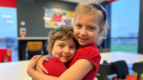 Lacie (left) and Betsy (right) at school. Both in red polo shirts and have short hair with headbands. 