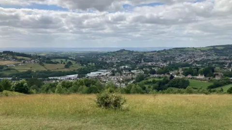 A view from the top of Rodborough Common. A town can be seen at the bottom of the hill, with rolling green fields visible far into the distance. 