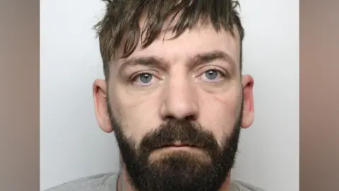 West Yorkshire Police A police mugshot of a man with brown hair and beard wearing a grey jumper