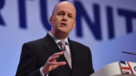 Sir Ashley Fox at the Conservative conference in Birmingham. He is stood on a stage, speaking.