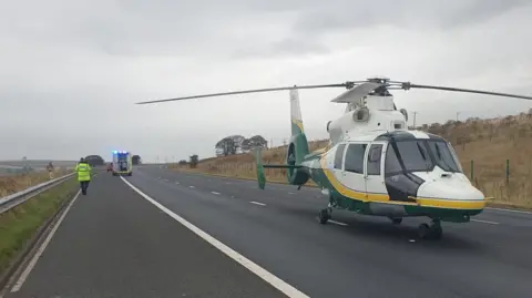 GNAAS A helicopter parked on a motorway. An ambulance is in the background with a person wearing a hi-vis jacket.