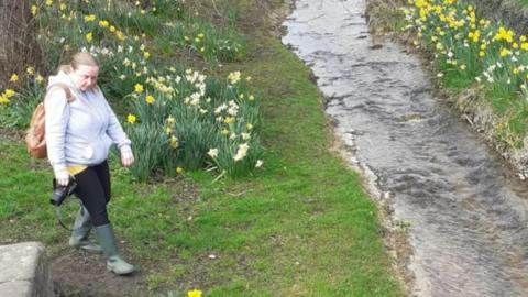 Elizabeth Cross walking in a field surrounded by daffodils and a stream
