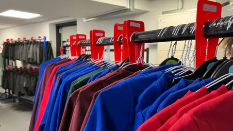 Inside a uniform exchange with rows of school sweatshirts, blazers and summer dresses hanging up different colours.