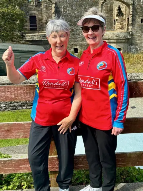 Two women standing and cheering, wearing red uniforms 