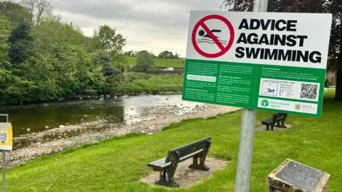 A sign saying Advice Against Swimming posted alongside a river in Lancashire. 