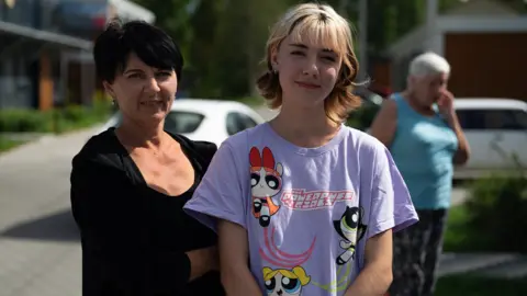Lee Durant/BBC Valeria (right) stands in a lilac Powerpuff Girls t-shirt with her mother in their refugee village
