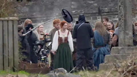 Peter Jolly/Northpix Karen Gillan filming at Eilean Donan Castle. She is wearing period clothing and is surrounded by other actors and members of the film crew.