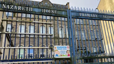 Shows a school with a gate giving the name as Nazareth House primary school