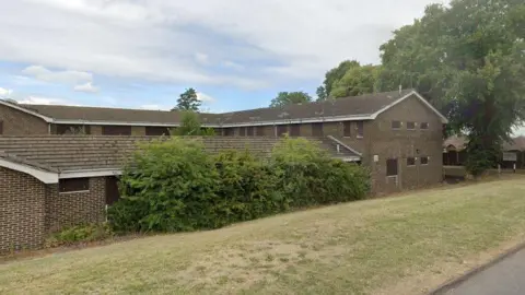 Google A derelict building with windows boarded up.