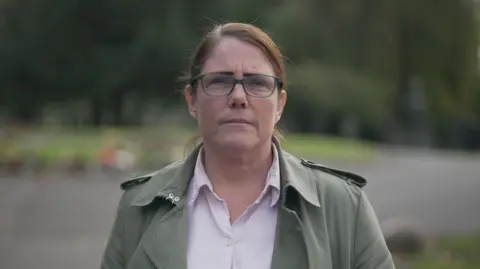 BBC/Brijesh Patel Kate Pollitt, with brown, swept back hair and wearing glasses, is photographed in a park. She wears a light green jacket and an open white shirt.