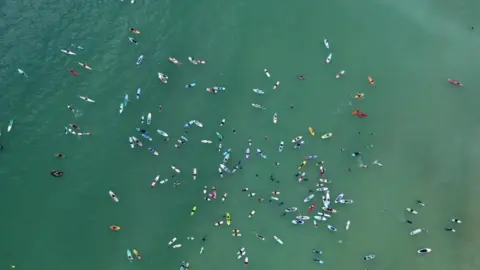 A drone shot of lots of swimmers and surfers in the water at Gylly beach. The sea looks a greenish blue.