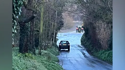 Maggie Carden A car driving towards a flooded section of the road.