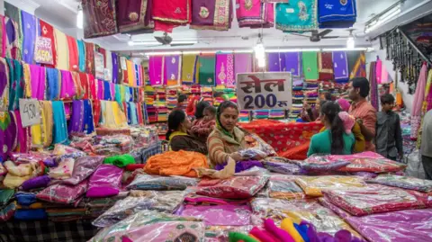 Universal Images Group via Getty Images A woman shopping in a colourful marketplace in Jaipur city, India, with a 'sale' placard behind her in Hindi. 