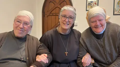 Anjana Gadgil/BBC The Poor Clares of Arundel: Sisters Aelred, Gabriel and Leo, sat together linking arms, dressed in their nun's habits