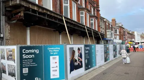 Andrew Turner/BBC Hoardings surround the facade of the old Palmers Department Store with wooden boards behind the iron pillars, and canopy above, and brickwork with bay windows above that. A man carrying a bag is walking down the pedestrianised King Street.