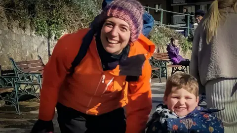 Family photo Sarah and Ivor are walking on a city street. Both are looking at the camera and smiling. they both have on winter coats