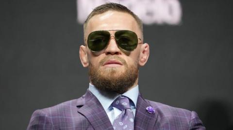 Conor McGregor in sunglasses and purple suit at a news conference