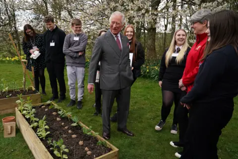 Getty Images King Charles with children from Robert Burns Academy in the grounds of Dumfries House in 2022. The pupils had been taking part in a food education programme delivered at the property. King Charles is standing next to a wooden planter containing potatoes.